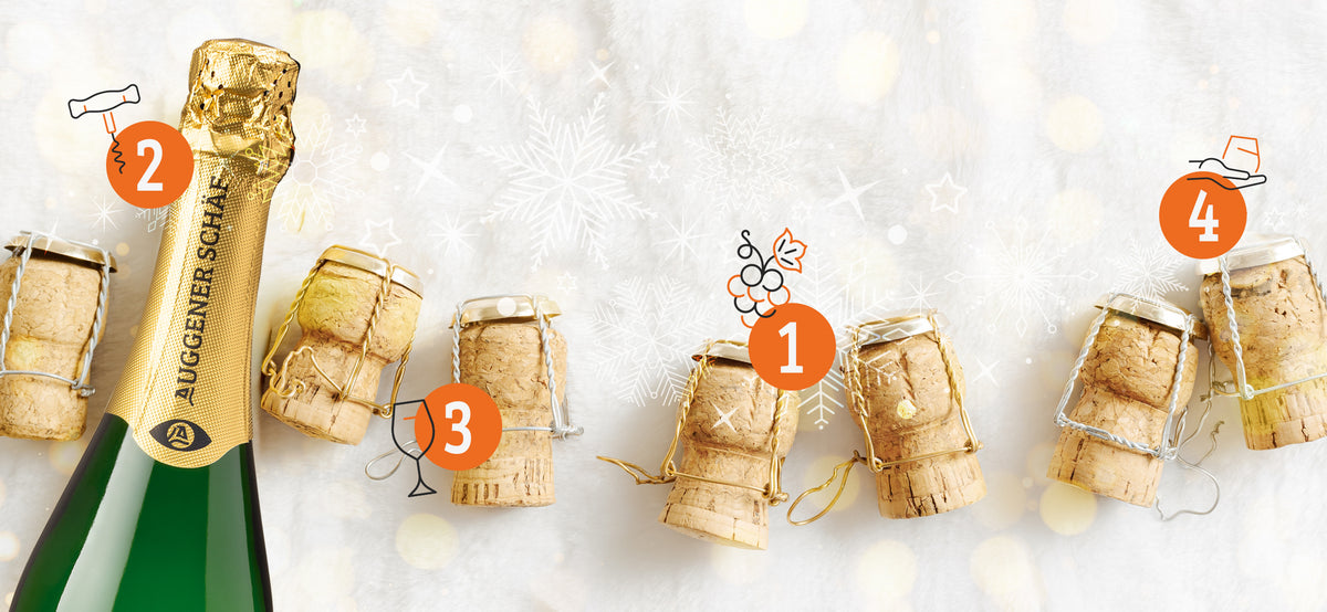 Festliche Szene eines Adventskalenders mit einer grünen Sektflasche 'Auggener Schaf' und mehreren Champagnerkorken auf weißem, flauschigem Untergrund. Schneeflocken und Sterne im Hintergrund erzeugen eine winterliche Feierstimmung.